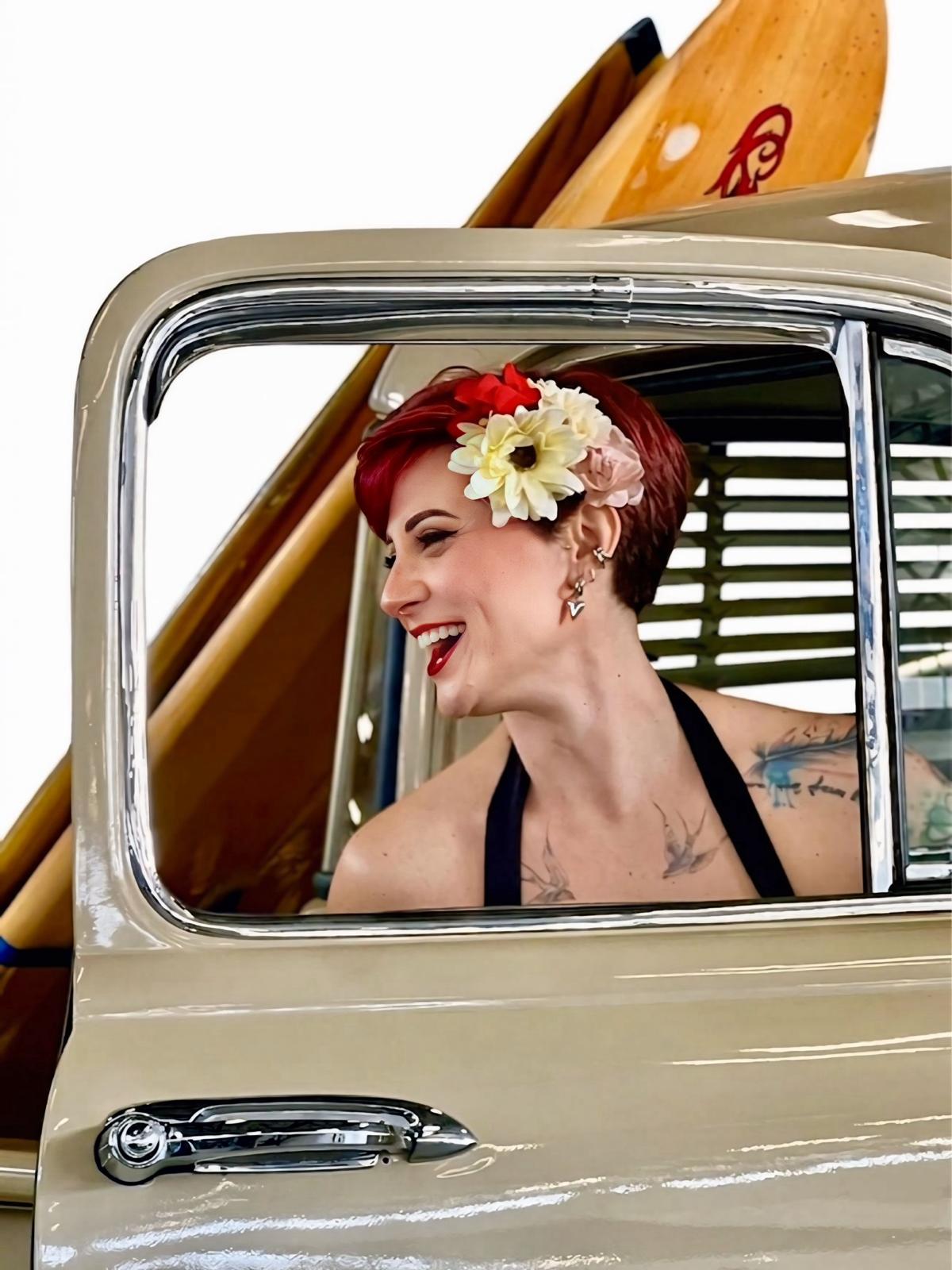 Look pin-up con fiori tra i capelli, affacciata al finestrino di un’auto d’epoca