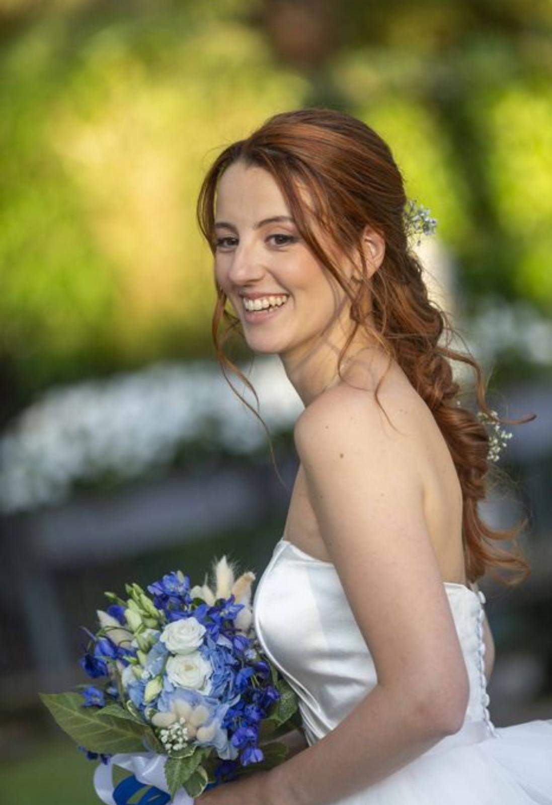 Sposa sorridente in giardino con bouquet blu e capelli raccolti