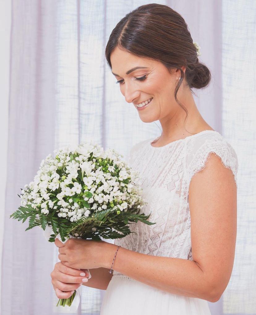 Sposa sorridente con bouquet di gypsophila, trucco naturale e chignon morbido