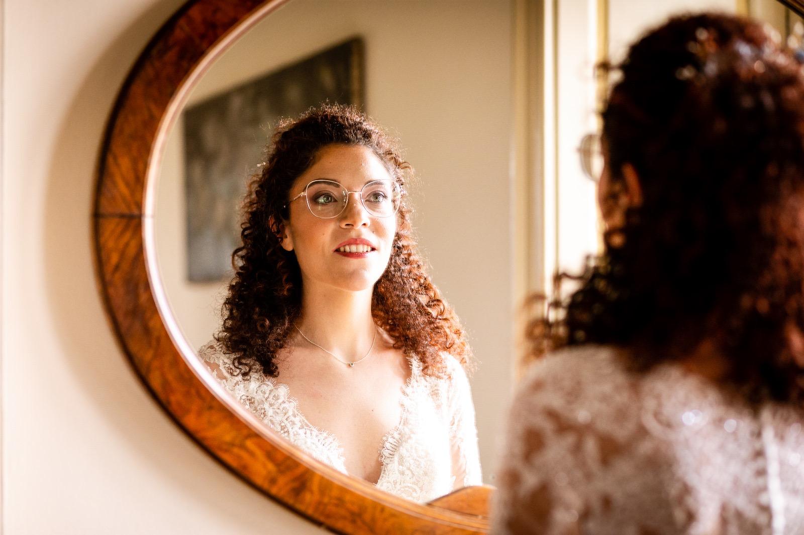 Sposa dai capelli ricci riflessa in uno specchio ovale durante la preparazione
